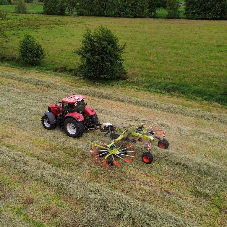 Nahaufnahme eines landwirtschaftlichen Geräts, das Gras auf einem Feld häuft.